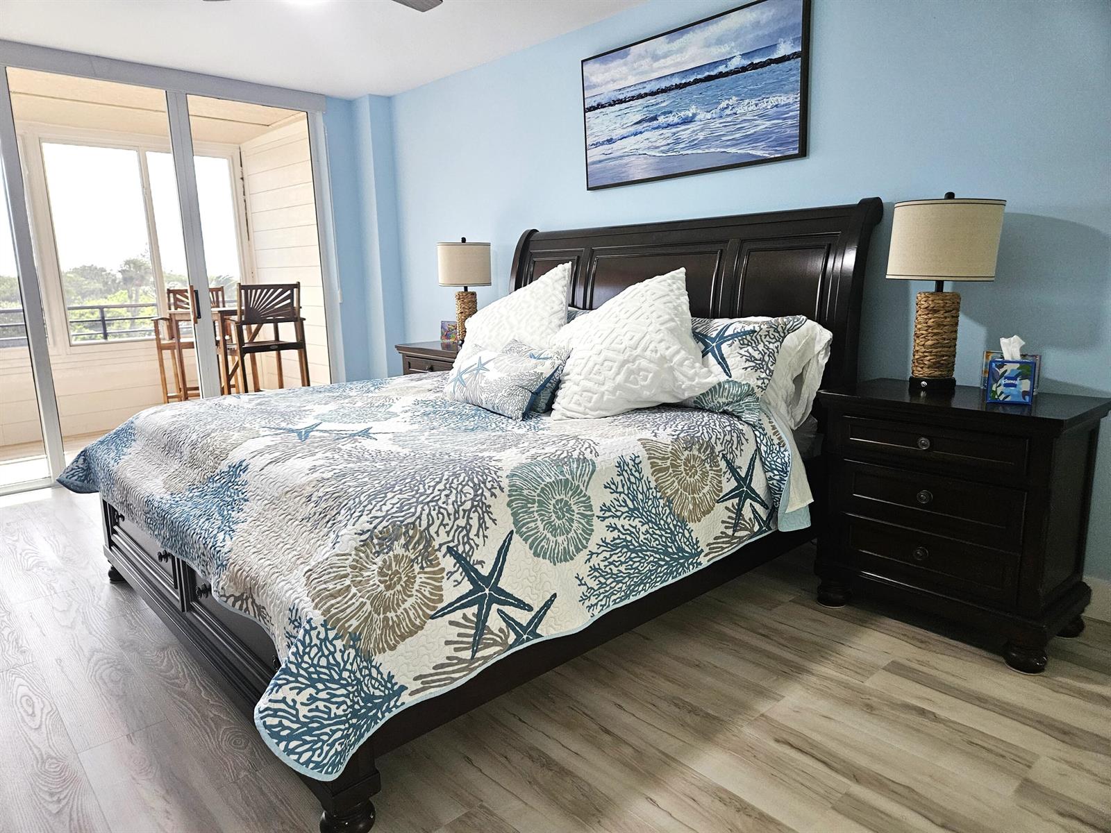 A bedroom features a dark wood bed frame, coastal-themed bedding, and a balcony with seating — 1357 NE Ocean Boulevard # 312, Stuart FL 34996, STUART, FL