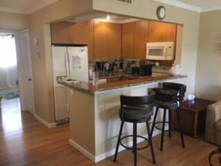 A kitchen with wood cabinets and a breakfast bar featuring two stools on wood flooring — 630 Snug Harbor Drive # C14, Boynton Beach FL 33435, BOYNTON BEACH, FL