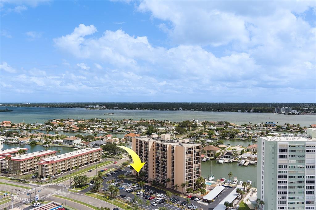 An aerial view shows a multi-story apartment building with a parking lot near water — 51 ISLAND WAY UNIT 101, CLEARWATER BEACH, FL