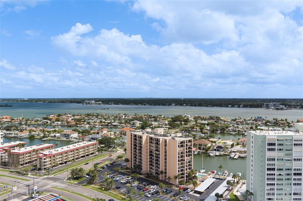 An elevated exterior view shows a coastal neighborhood with apartment buildings, a parking lot, and water — 51 ISLAND WAY UNIT 101, CLEARWATER BEACH, FL