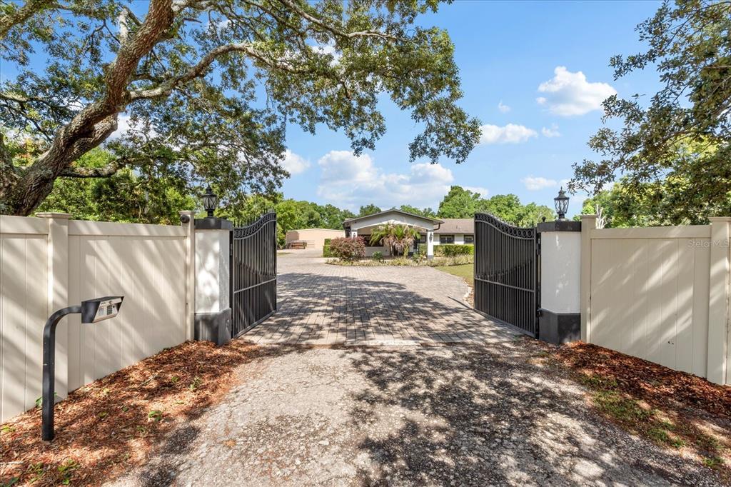 An open black metal gate leads to a paved driveway and a single-story house — 524 EDEN PARK, ALTAMONTE SPRINGS, FL