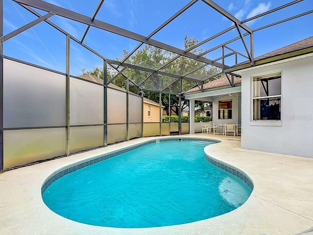 A swimming pool with a screen enclosure sits on a patio next to a house — 644 MONTARA DR, DAVENPORT, FL