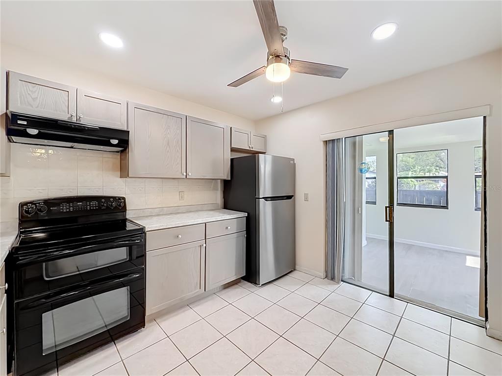 A kitchen features gray cabinets, stainless steel appliances, tile flooring, and a sliding glass door — 55 SEMINOLE DRIVE, ROYAL PALM BEACH, FL