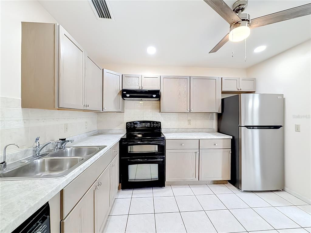 A kitchen features light wood cabinets, white countertops, a black stove, and a stainless refrigerator — 55 SEMINOLE DRIVE, ROYAL PALM BEACH, FL