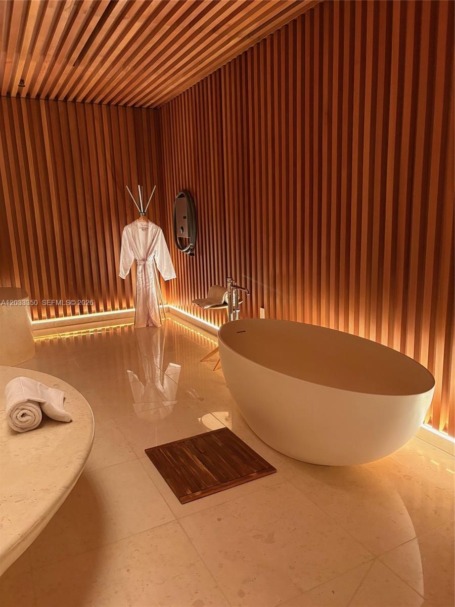 A modern bathroom features a freestanding tub, wood-slatted walls, and a hanging robe — MIAMI BEACH, FL