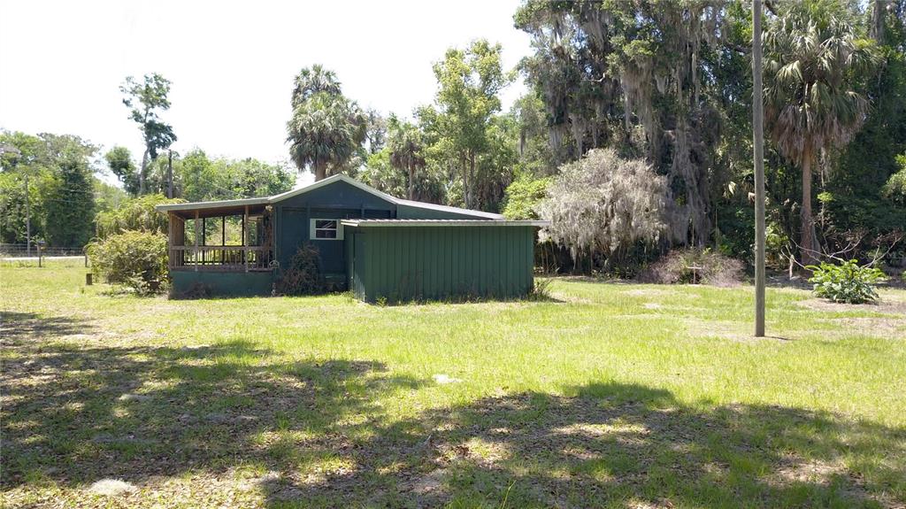 A green cabin with a screened porch sits on a grassy lot with trees — 11291 SE 202ND LANE, INGLIS, FL