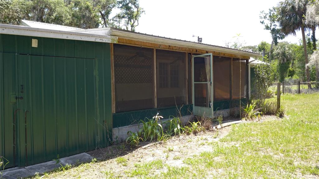A green metal-sided structure features a screened-in porch with a door and a concrete foundation — 11291 SE 202ND LANE, INGLIS, FL