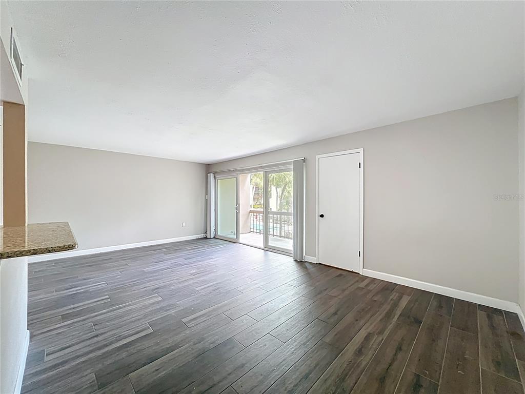 An empty living room features dark wood-look tile flooring, light gray walls, and sliding glass doors — 590 ORANGE DRIVE UNIT 136, ALTAMONTE SPRINGS, FL