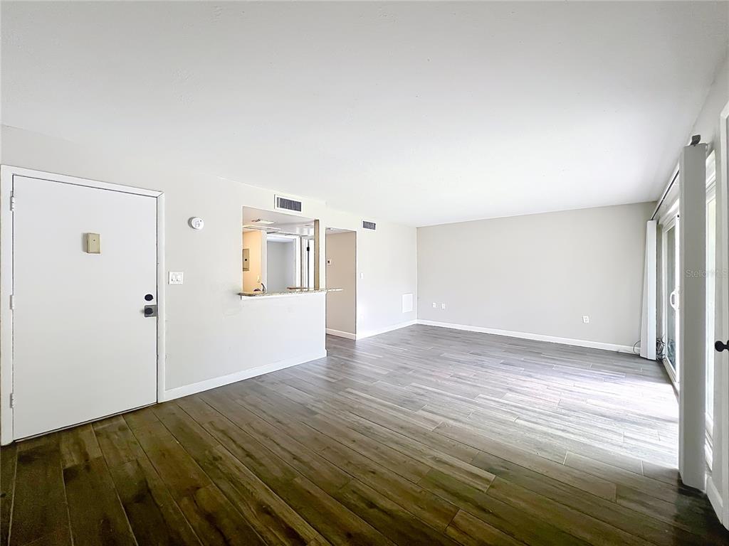 An empty living room features wood-look flooring, a pass-through kitchen window, and sliding glass doors — 590 ORANGE DRIVE UNIT 136, ALTAMONTE SPRINGS, FL