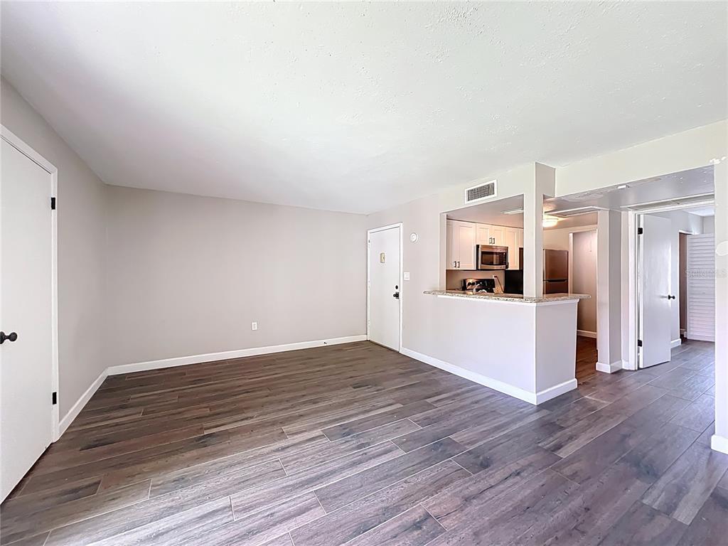 An unfurnished living area features wood-look tile flooring, light gray walls, and an open kitchen — 590 ORANGE DRIVE UNIT 136, ALTAMONTE SPRINGS, FL