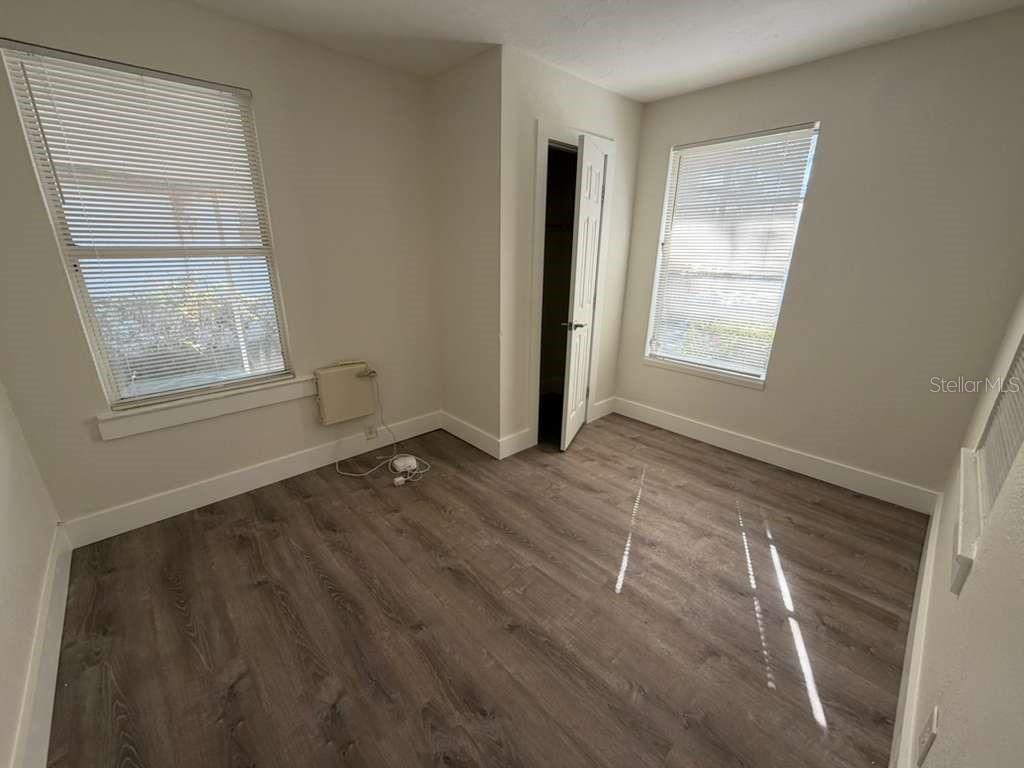 An empty bedroom features light-colored walls, wood-look flooring, two windows with blinds, and a doorway — 3404 E 33RD AVENUE, TAMPA, FL