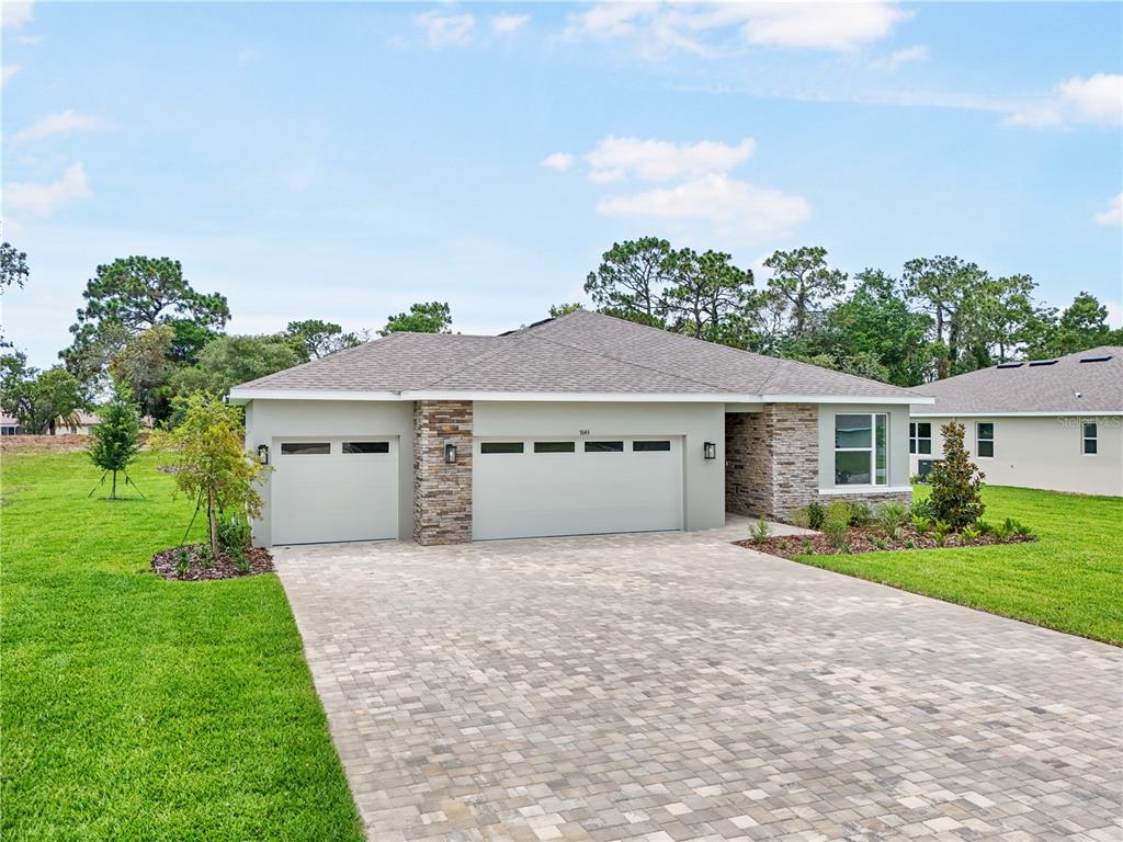 A single-story house with a three-car garage, stone accents, and a paved driveway — 9143 PLAYERS DRIVE, WEEKI WACHEE, FL