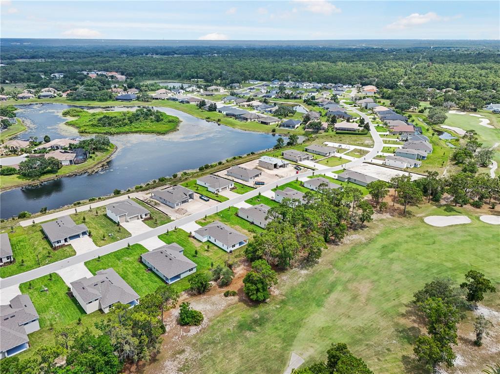 An aerial view shows a suburban neighborhood with houses bordering a lake and golf course — 9143 PLAYERS DRIVE, WEEKI WACHEE, FL