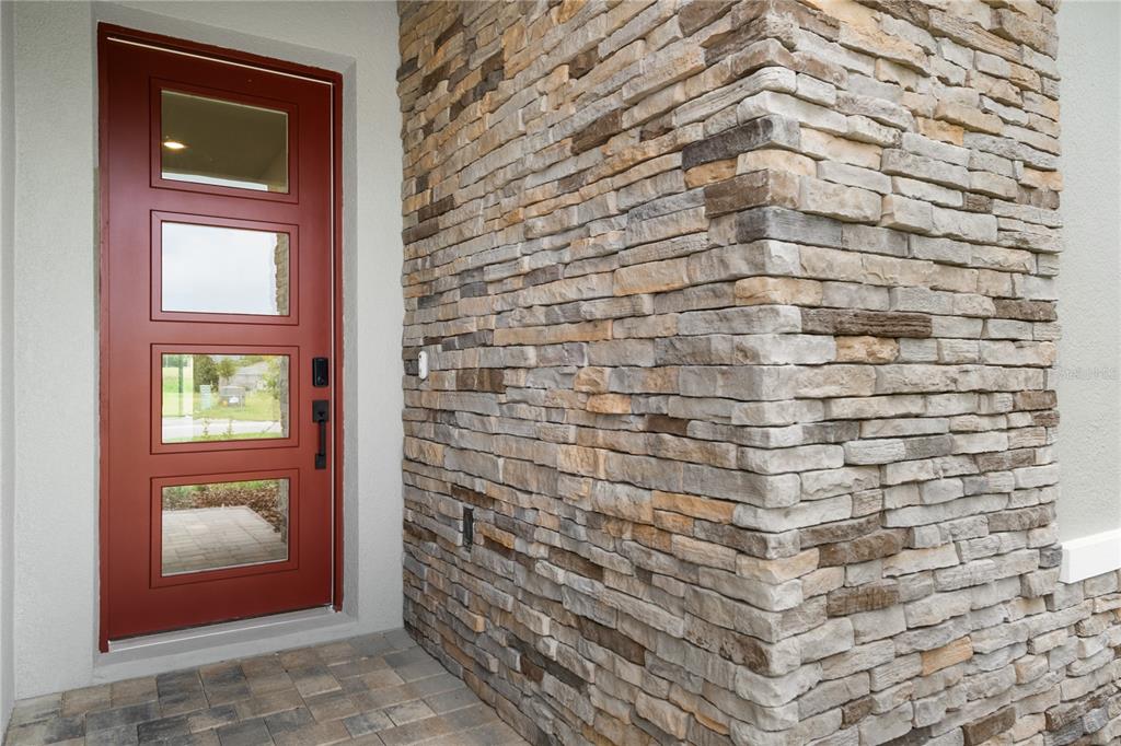 A red front door with four glass panels sits beside a stone-clad exterior wall — 9143 PLAYERS DRIVE, WEEKI WACHEE, FL