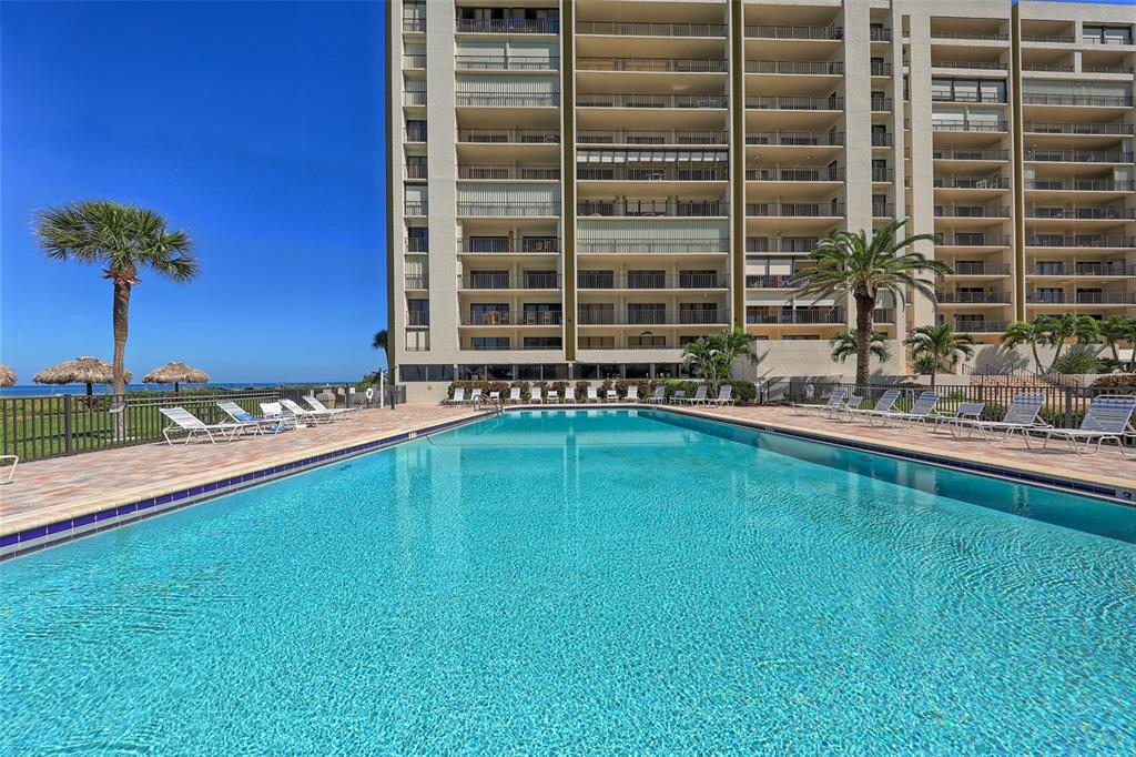 A large swimming pool sits in front of a multi-story residential building with balconies — 1480 GULF BOULEVARD UNIT 512, CLEARWATER, FL