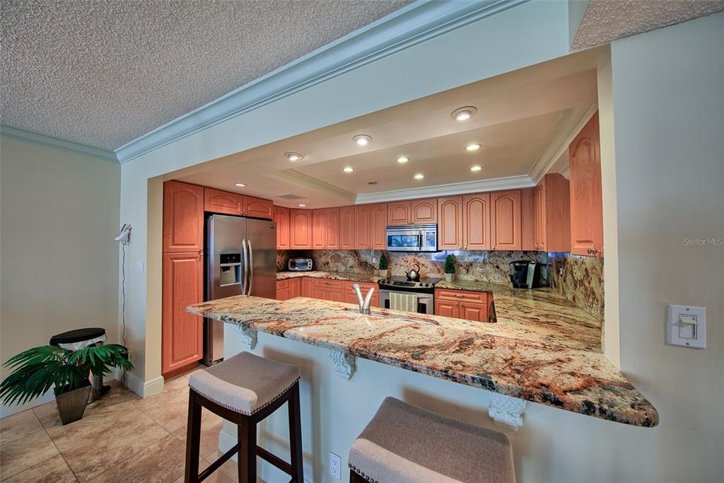 A kitchen features wood cabinets, granite countertops, a breakfast bar with stools, and recessed lighting — 1480 GULF BOULEVARD UNIT 512, CLEARWATER, FL