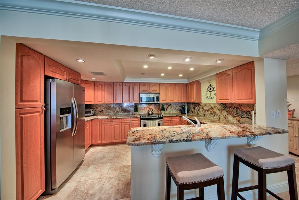 A kitchen features wood cabinets, granite countertops, stainless steel appliances, and a breakfast bar — 1480 GULF BOULEVARD UNIT 512, CLEARWATER, FL
