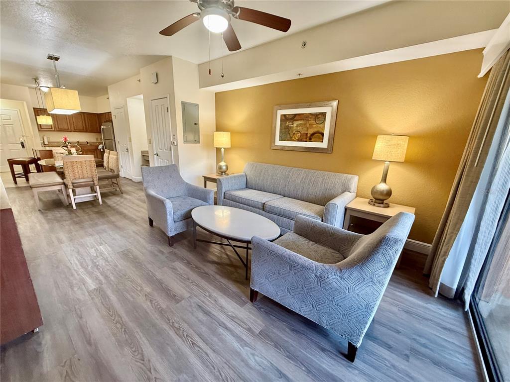 A living room with gray furniture, wood-look flooring, and a dining area in the background — 12539 FLORIDAYS RESORT DRIVE UNIT 107D, ORLANDO, FL