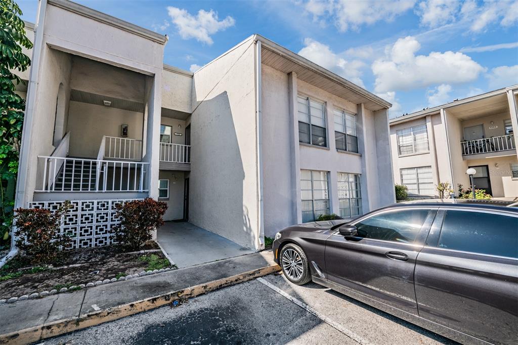 A two-story apartment building exterior features a concrete walkway, white railings, and a parked car — 2625 STATE ROAD 590 UNIT 2714, CLEARWATER, FL