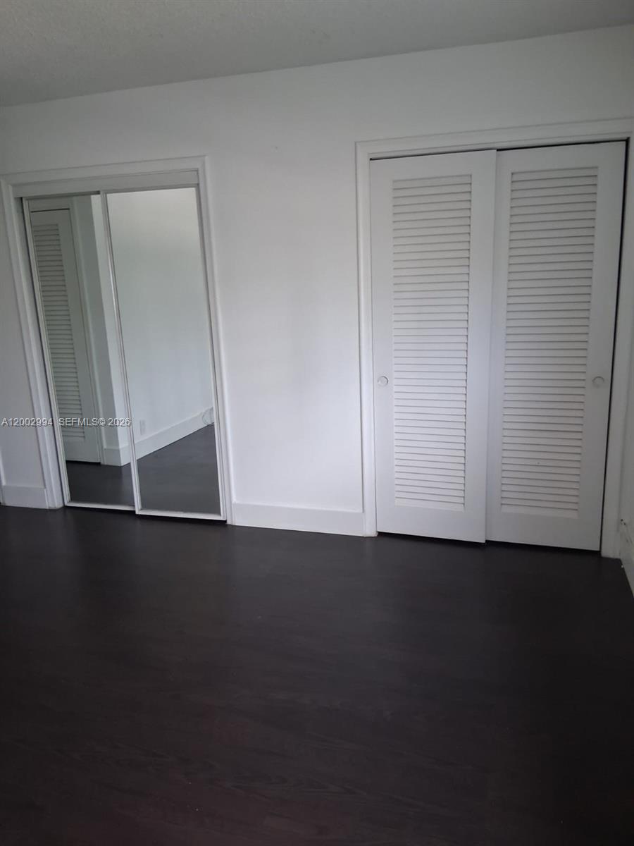 A room features dark wood flooring, a mirrored sliding closet, and a white louvered closet door — 301 NE 14th Ave # 202, Hallandale Beach FL 33009, HALLANDALE BEACH, FL