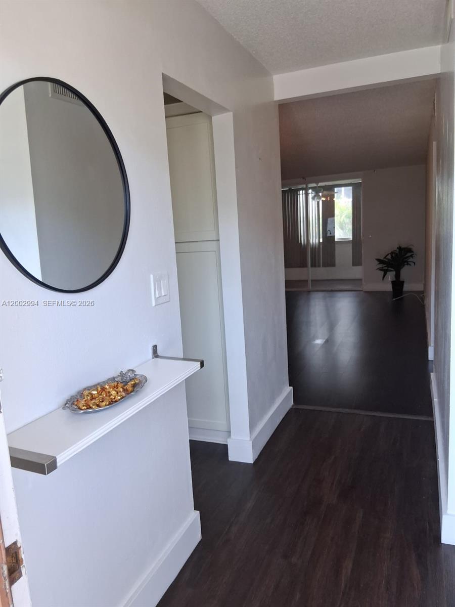 A hallway with dark flooring leads to a living area featuring a round wall mirror — 301 NE 14th Ave # 202, Hallandale Beach FL 33009, HALLANDALE BEACH, FL