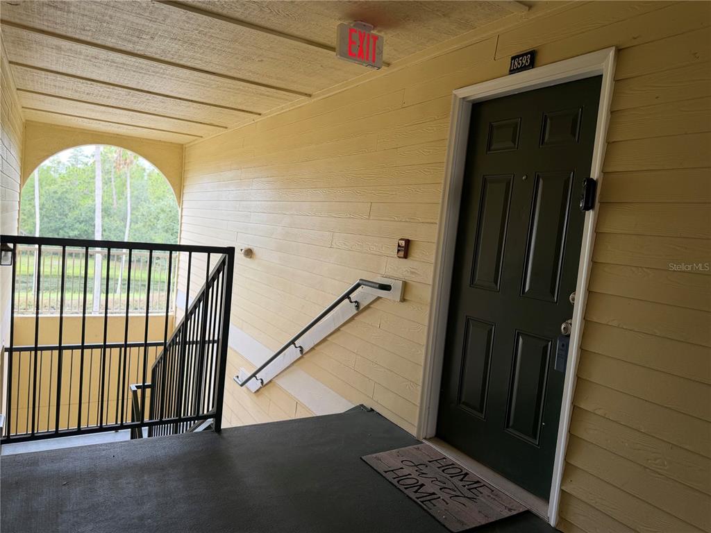 An exterior apartment landing features a dark door, a metal railing, and a welcome mat — 18593 BRIDLE CLUB DRIVE, TAMPA, FL