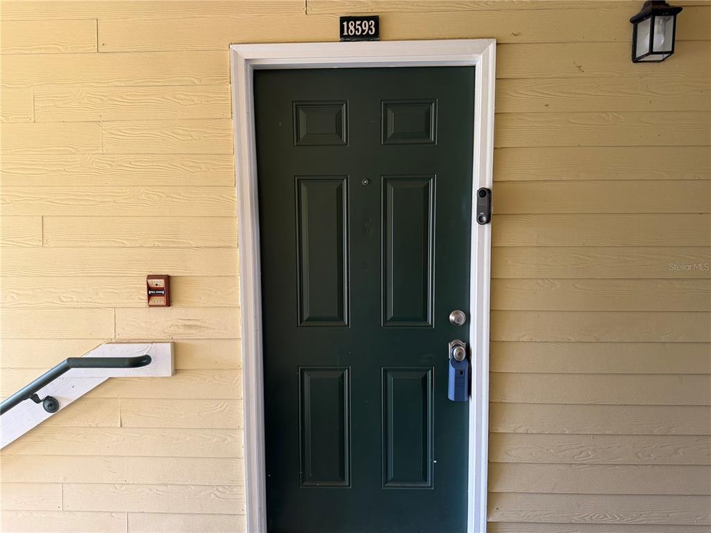 A dark green front door with a smart lock is set in light yellow siding — 18593 BRIDLE CLUB DRIVE, TAMPA, FL