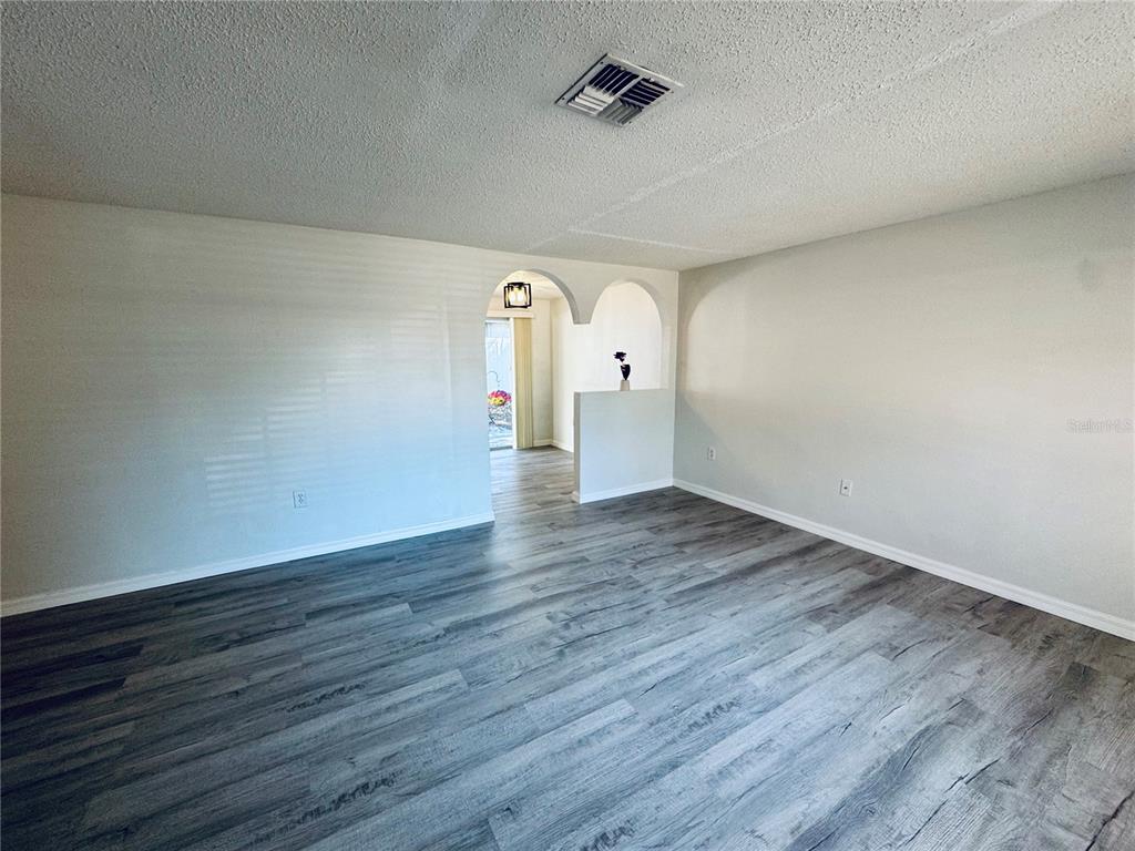 An empty living room features gray wood-look flooring, white walls, and an arched entryway — 7116-7118 GREEN STREET, NEW PORT RICHEY, FL