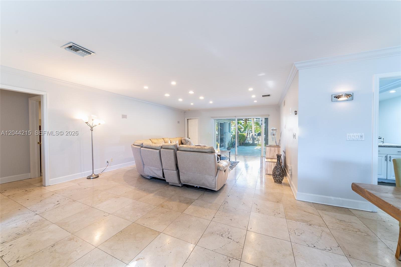 A spacious living room features light-colored tile flooring, a large sectional sofa, and sliding glass doors — 13140 Coronado Dr, North Miami FL 33181, NORTH MIAMI, FL