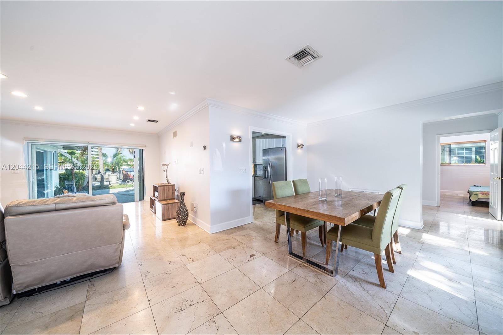 A dining area with a wooden table and green chairs sits beside a living space — 13140 Coronado Dr, North Miami FL 33181, NORTH MIAMI, FL