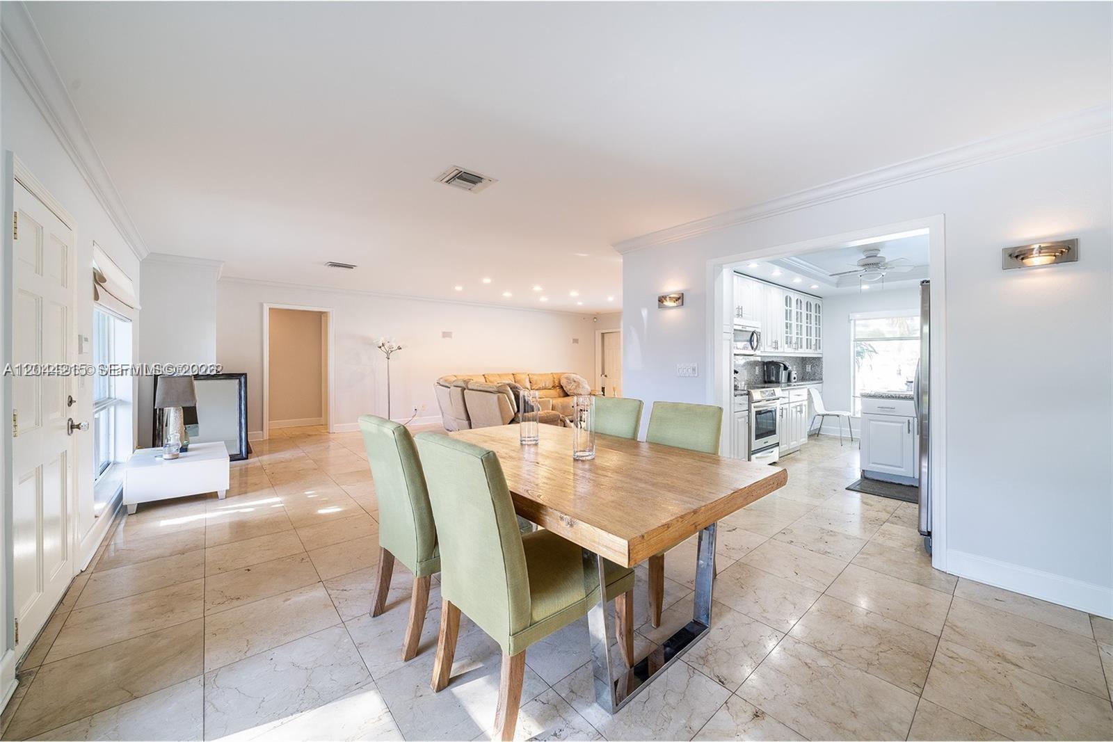 A dining area with a wooden table and green chairs sits before an open kitchen — 13140 Coronado Dr, North Miami FL 33181, NORTH MIAMI, FL