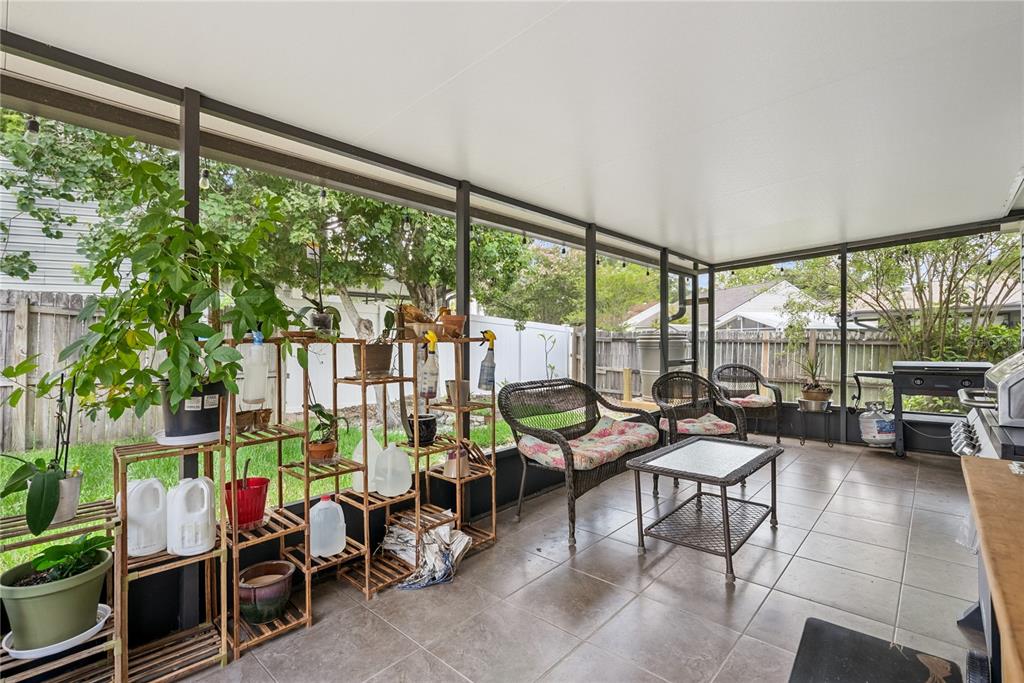 A screened-in patio features tiled flooring, a wooden plant stand, and outdoor seating — 1009 MCCULLY COURT, OVIEDO, FL
