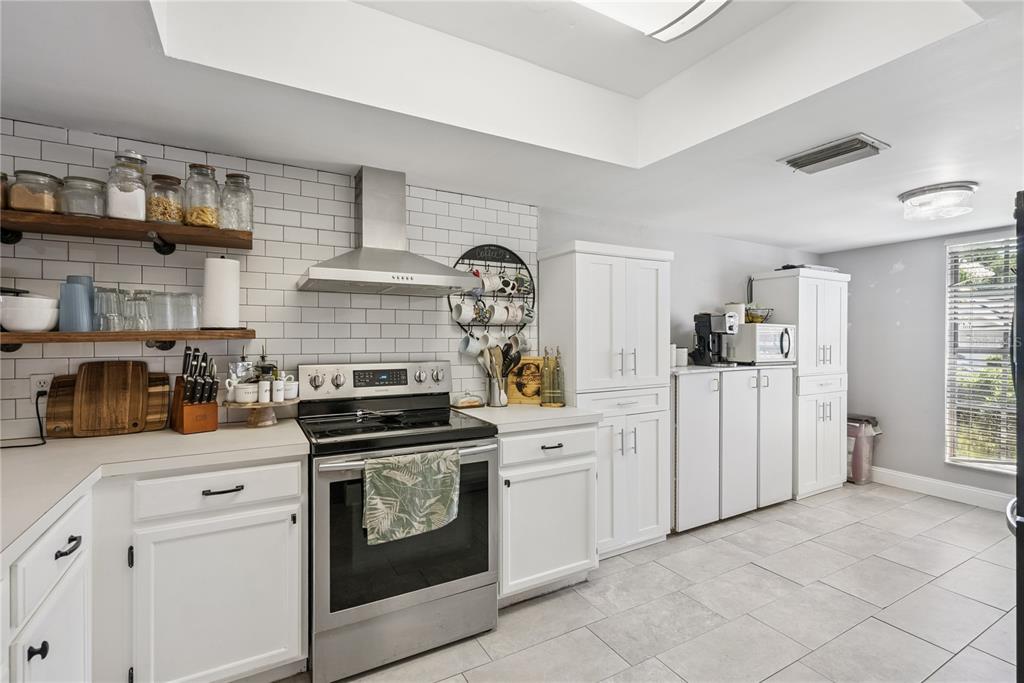 A kitchen features white cabinets, stainless steel appliances, open shelving, and a subway tile backsplash — 1009 MCCULLY COURT, OVIEDO, FL