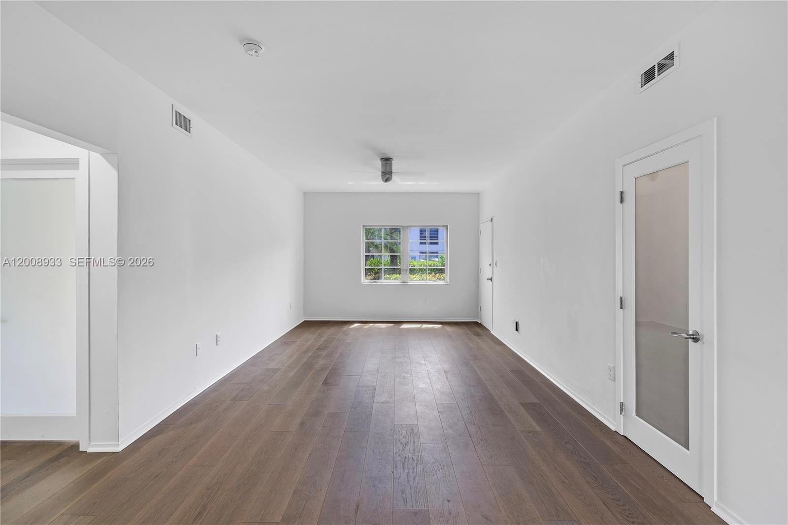An empty room features white walls, dark wood-look flooring, and a single window — 1600 Michigan Ave # 2, Miami Beach FL 33139, MIAMI BEACH, FL