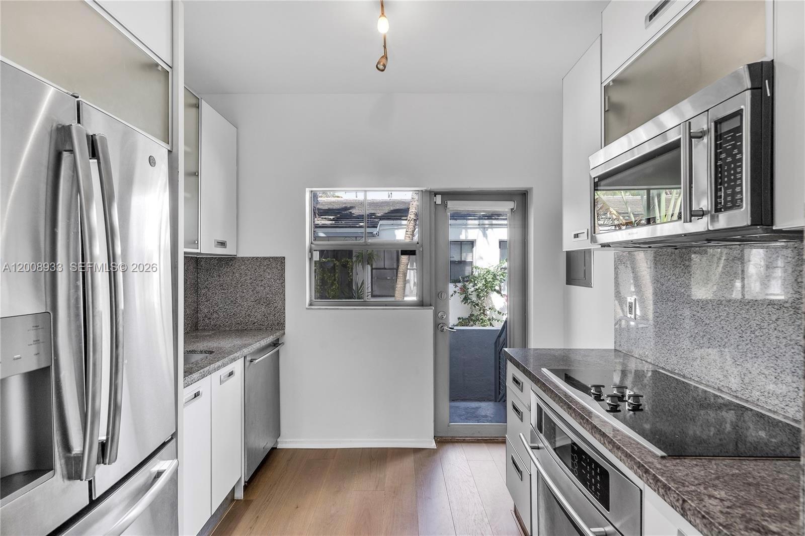 A galley kitchen features stainless steel appliances, granite countertops, white cabinetry, and a glass-paned door — 1600 Michigan Ave # 2, Miami Beach FL 33139, MIAMI BEACH, FL