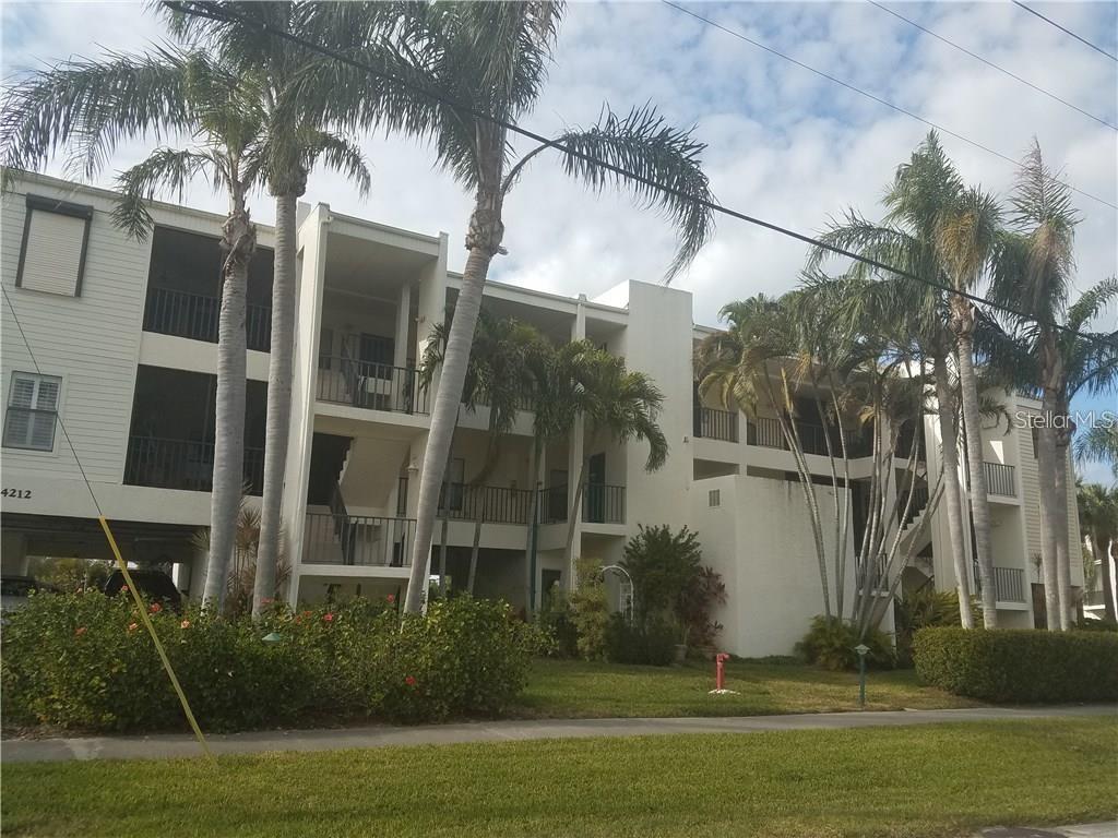 A three-story apartment building with white siding, balconies, and surrounding palm trees — 4212 126TH STREET W UNIT 407, CORTEZ, FL