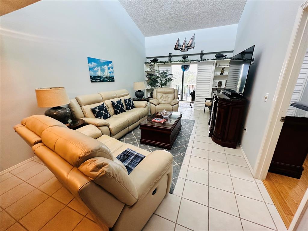 A living room features light-colored leather sofas, a dark wood coffee table, and tile flooring — 4212 126TH STREET W UNIT 407, CORTEZ, FL