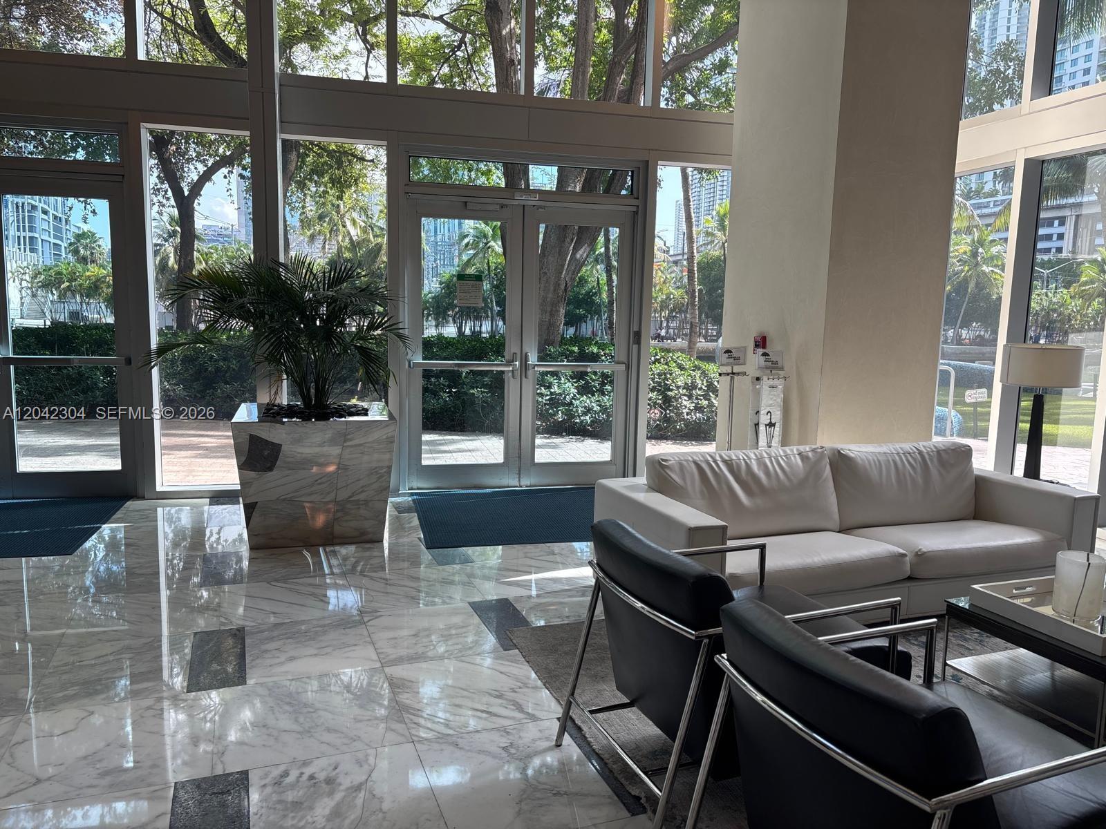 A lobby features marble floors, a white sofa, black armchairs, and glass doors to outside — 185 SW 7th St # 1410, Miami FL 33130, MIAMI, FL