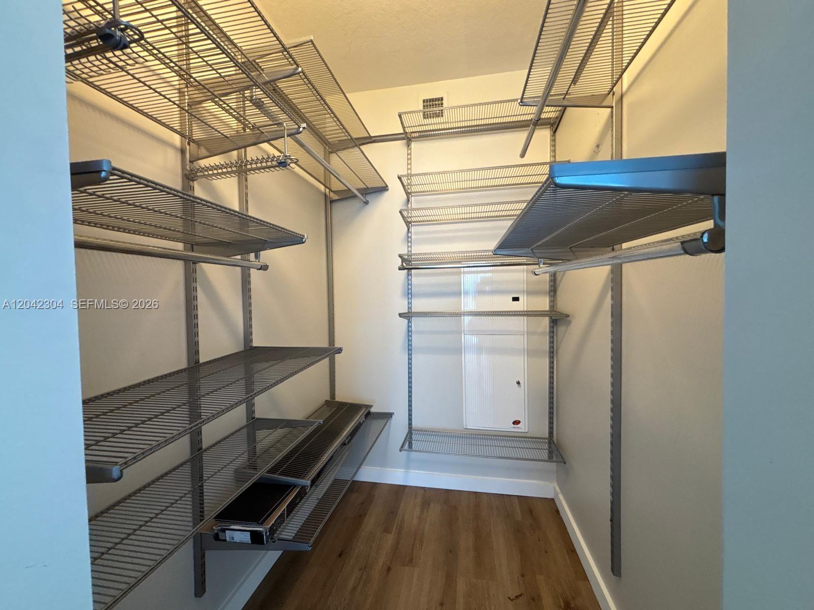 A walk-in closet features wire shelving units installed on the walls over wood-look flooring — 185 SW 7th St # 1410, Miami FL 33130, MIAMI, FL