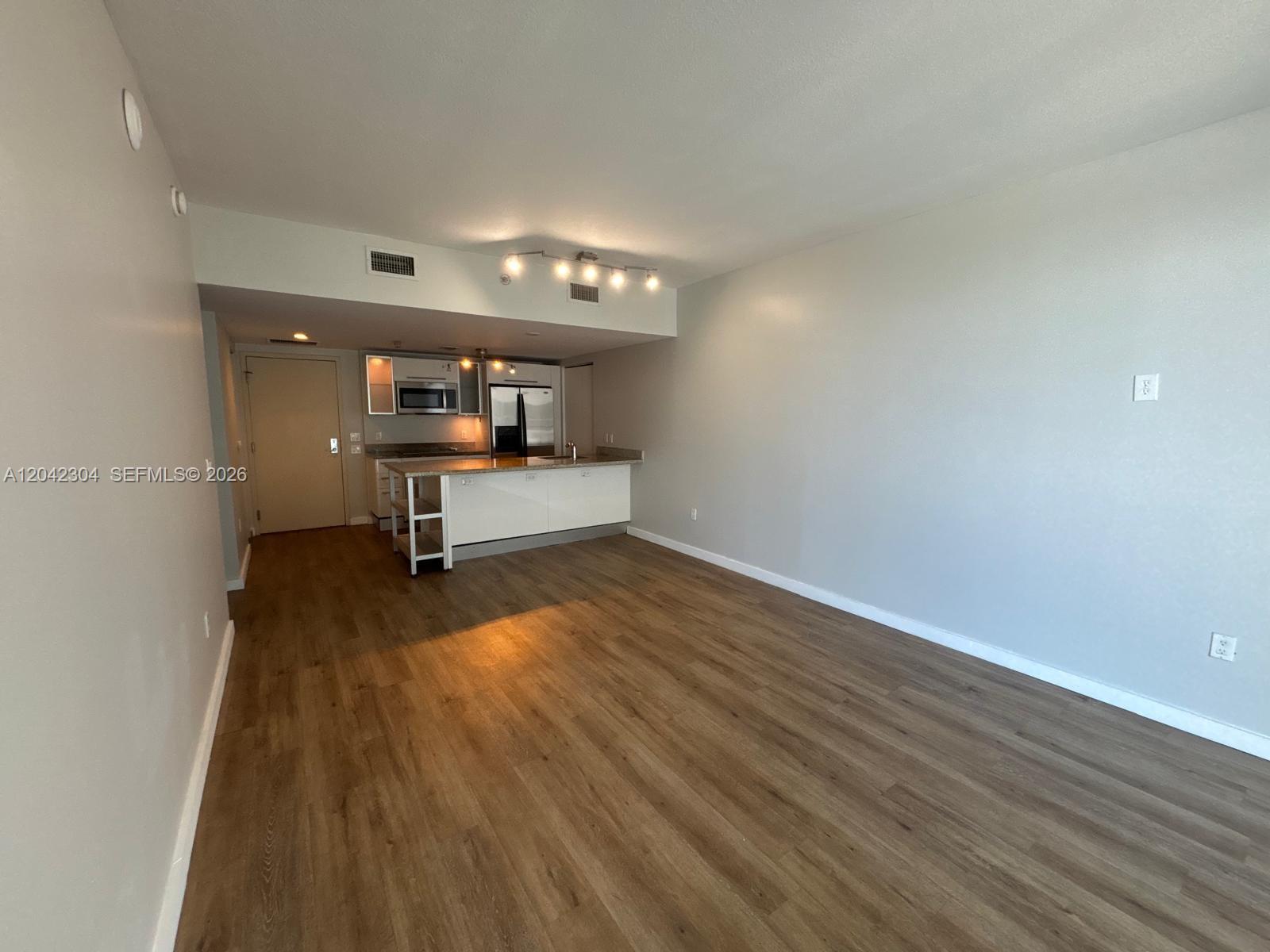 An open-concept living area features wood-look flooring and a kitchen with white cabinetry — 185 SW 7th St # 1410, Miami FL 33130, MIAMI, FL