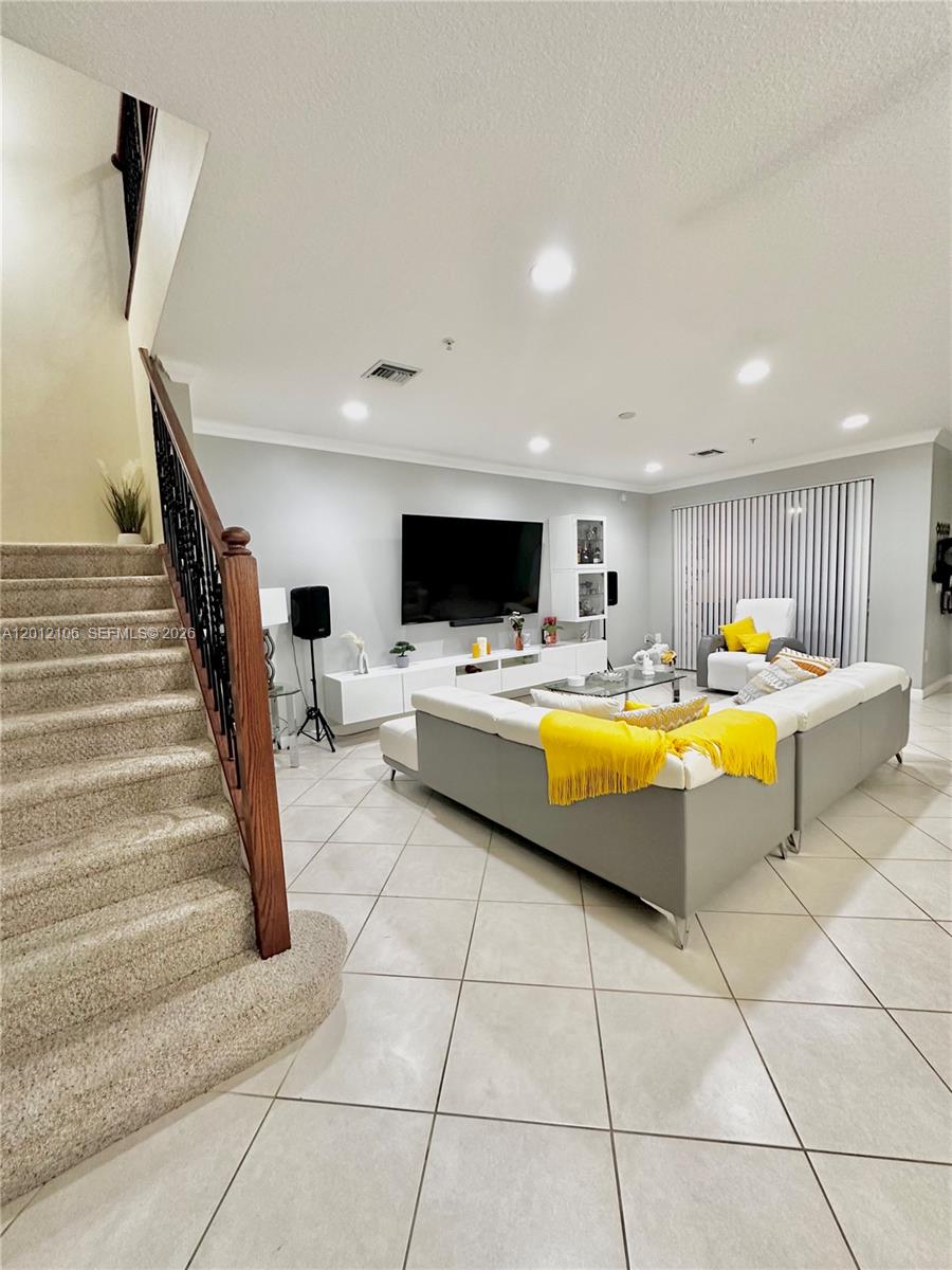 A living room features a large sectional sofa, a wall-mounted television, and carpeted stairs — 2900 NW 125th Ave # 105, Sunrise FL 33323, SUNRISE, FL