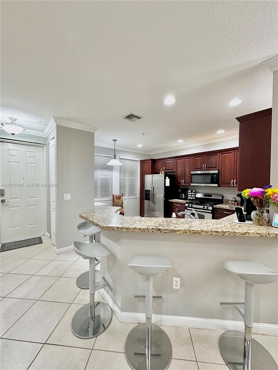 A kitchen features dark wood cabinets, granite countertops, a breakfast bar, and three bar stools — 2900 NW 125th Ave # 105, Sunrise FL 33323, SUNRISE, FL