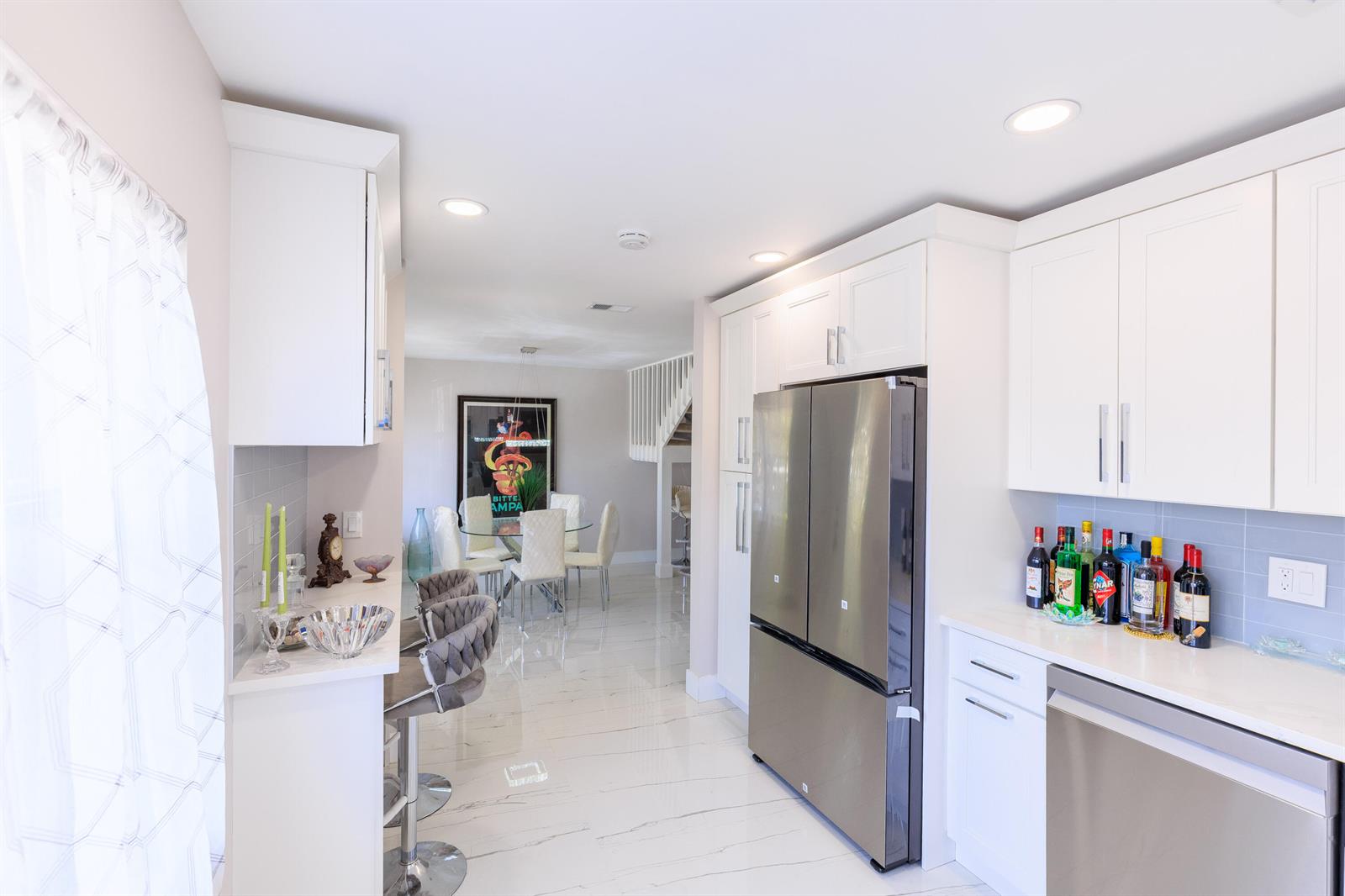 A modern kitchen features white cabinetry, stainless steel appliances, and a breakfast bar with stools — 5241 Jog Lane, Delray Beach FL 33484, DELRAY BEACH, FL