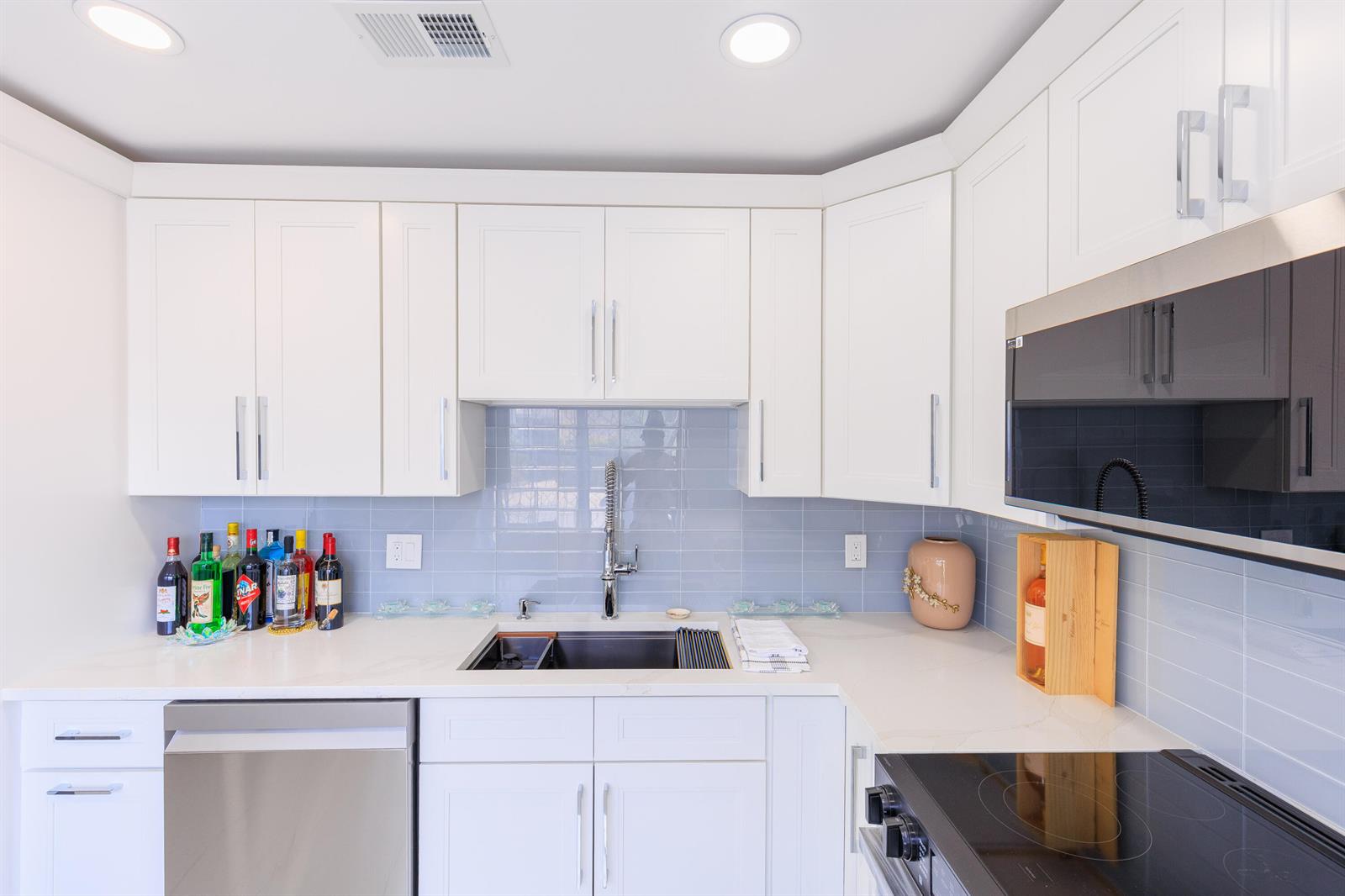 A kitchen features white cabinets, a light blue tiled backsplash, and a stainless steel sink — 5241 Jog Lane, Delray Beach FL 33484, DELRAY BEACH, FL