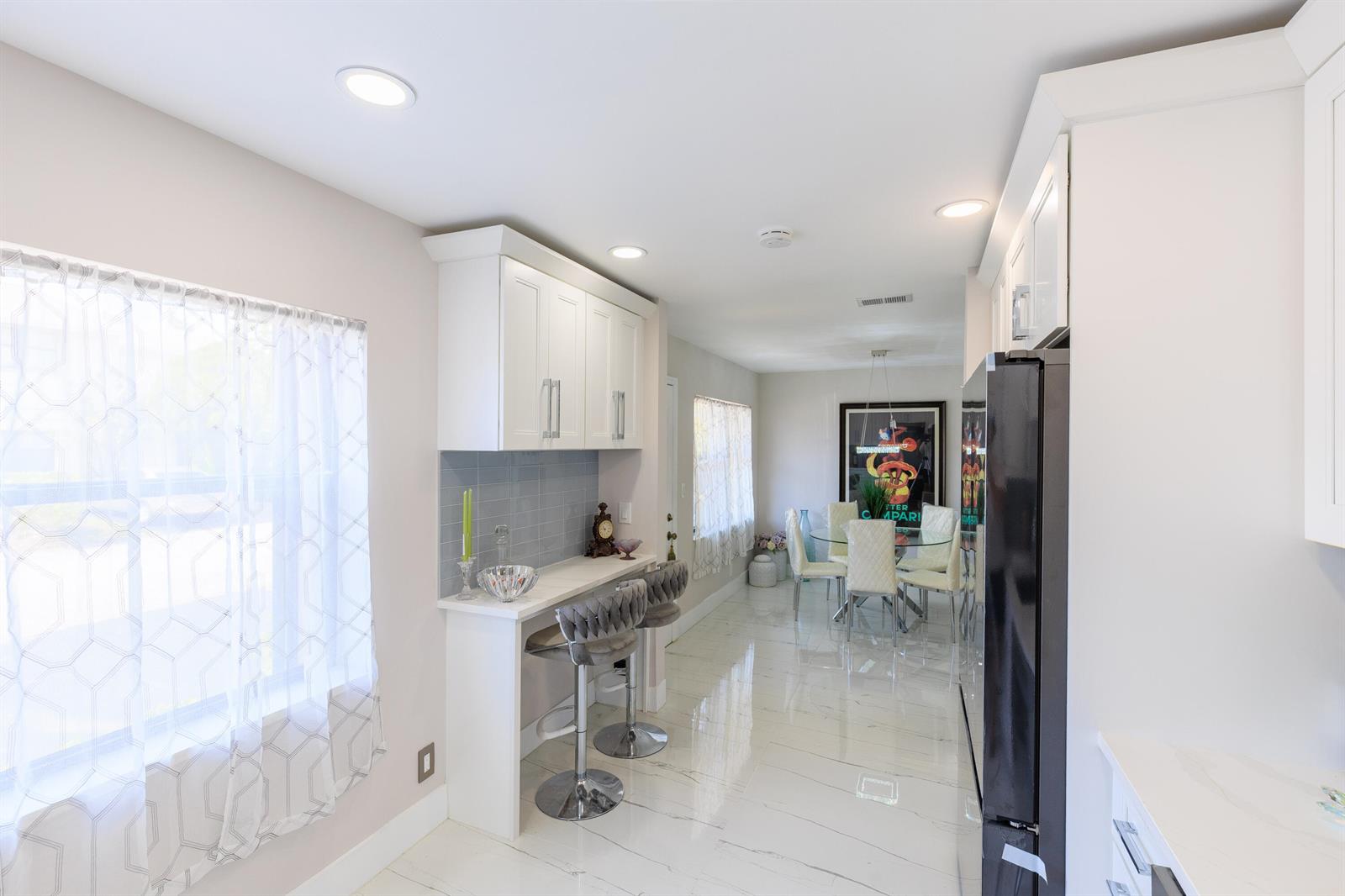 A kitchen features white cabinetry, a breakfast bar with two stools, and a dining area — 5241 Jog Lane, Delray Beach FL 33484, DELRAY BEACH, FL