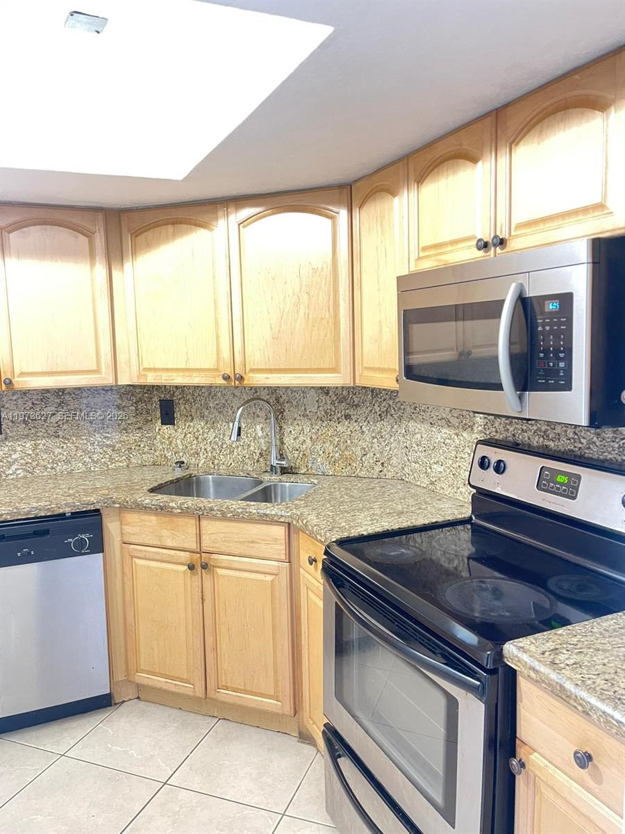 A kitchen features light wood cabinets, granite countertops, stainless steel appliances, and a tile floor — 7410 SW 82nd St # K202, Miami FL 33143, MIAMI, FL
