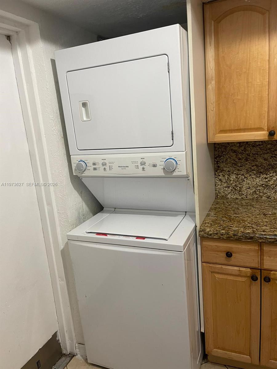 A white stacked Frigidaire washer and dryer unit sits next to wooden kitchen cabinets — 7410 SW 82nd St # K202, Miami FL 33143, MIAMI, FL