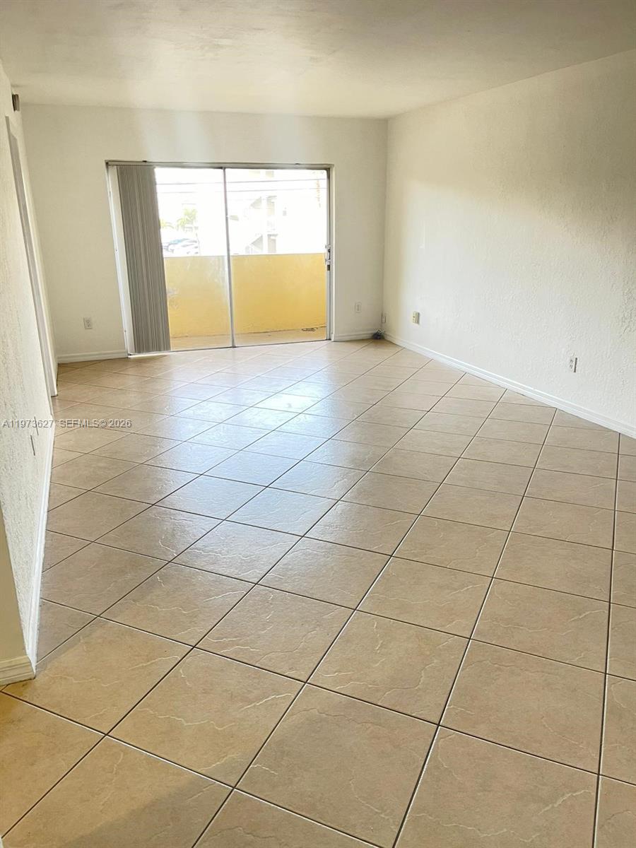 An empty living room features beige tile flooring and a sliding glass door to a balcony — 7410 SW 82nd St # K202, Miami FL 33143, MIAMI, FL