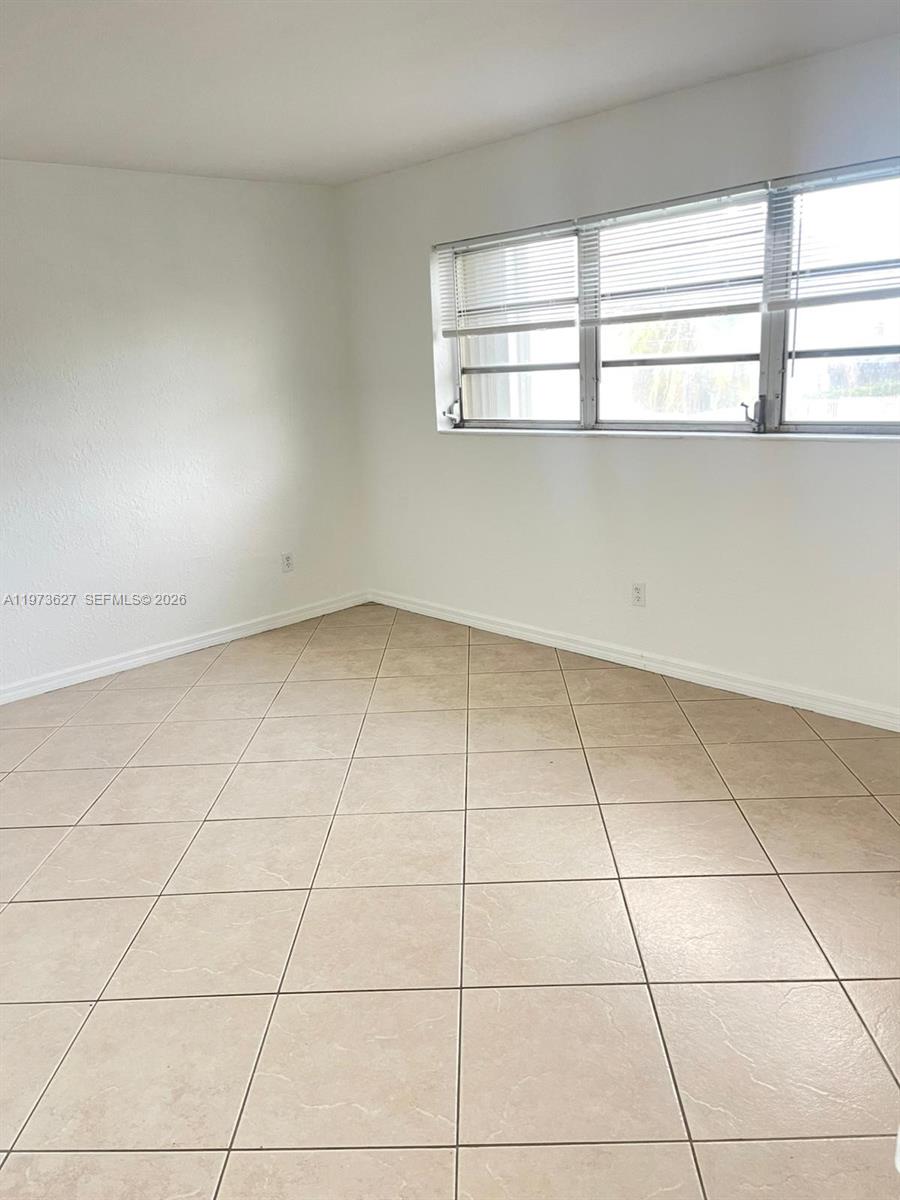 An empty room features white walls, beige tile flooring, and a window with blinds — 7410 SW 82nd St # K202, Miami FL 33143, MIAMI, FL