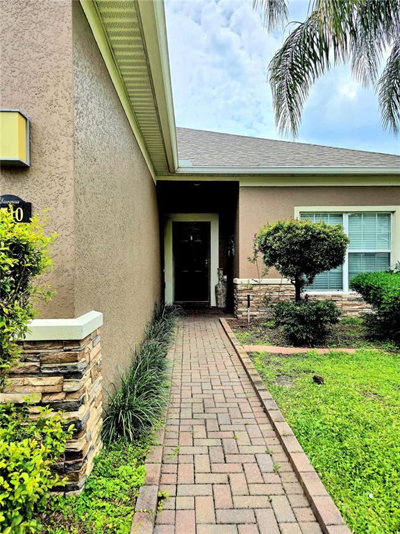 A brick walkway leads to the dark front door of a tan house with stone accents — 1710 PLANTATION POINTE DRIVE, ORLANDO, FL